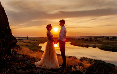 Loving couple, boyfriend and girlfriend looking at each other   at sunset on the mountain on the background of the river
