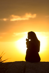 silhouette of beautiful thoughtful girl sitting on the sand and enjoying the sunset, the figure of...