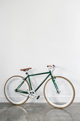 Fototapeta na wymiar Fixed Green and Brown Bicycle in Modern Home, Fixie Bike inside hous​e, white wall background, isolated retro bicycle 
