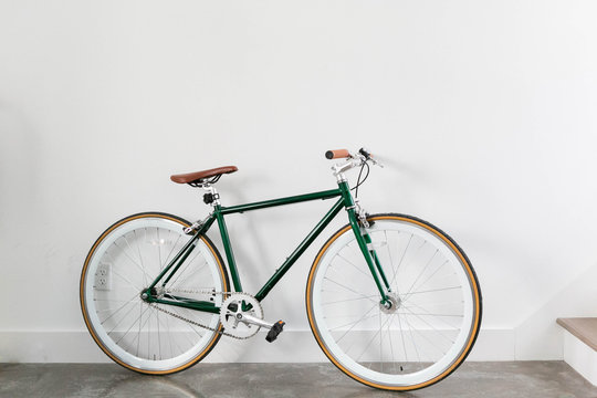 Fixed Green And Brown Bicycle In Modern Home, Fixie Bike Inside Hous​e, White Wall Background, Isolated Retro Bicycle 