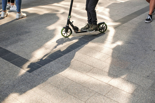 Photo of a scooter and human legs in different shoes walking on the sidewalk on the street