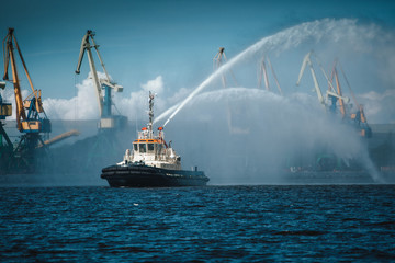 Naklejka na ściany i meble A firefighter floating modern tug boat sprays jets of water