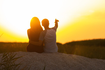silhouette of a loving couple at sunset sitting on sand on the beach, the figure of a man and a...