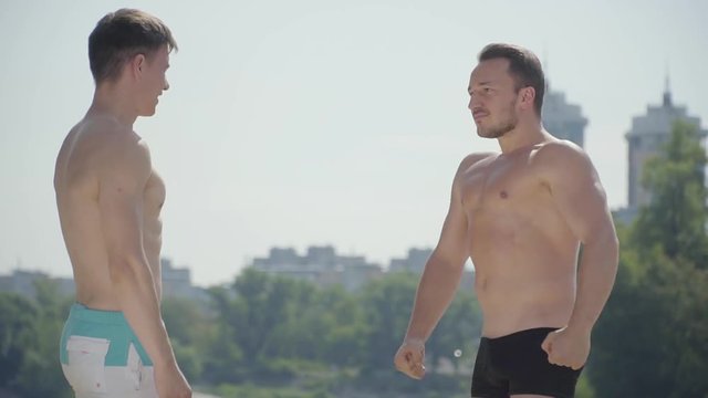 Athletic guys having fun outdoors. Men demonstrating muscles to each other. Sporty people with hot bodies resting outdoors. Bragging concept. Beautiful landscape