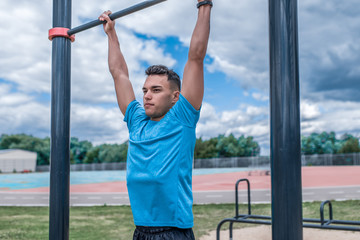 Fototapeta premium young guy, man sports athlete, in summer in city on sports ground, pulls up on bar, workout fitness, workout healthy lifestyle. Sportswear, strength and endurance, motivation.
