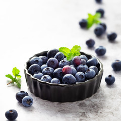Fresh ripe garden blueberries with sprigs of mint in a black baking bowl against grey concrete background