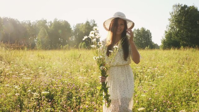 Cheerful woman in straw hat with flowers in the meadow