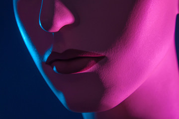 The nose and lips of the dummy. Part of face. Female robot. A woman's face in neon light. Artificial person. Cyberwoman. Plastic dummy. Doll