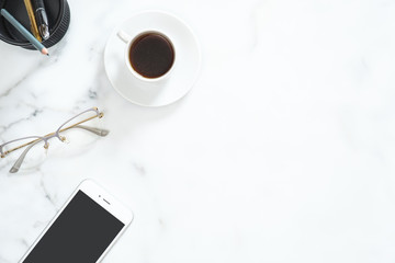 Modern home office desk workspace with coffee cup, mobile phone, glasses, stationery set on white marble stone background. Flatlay, top view, copy space. Beauty blogger workplace concept.