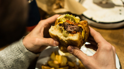 Young man's hands are holding a bitten hamburger in a fast food restaurant