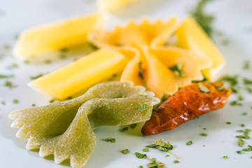 Different types of raw pasta on a plate with a cayenne pepper