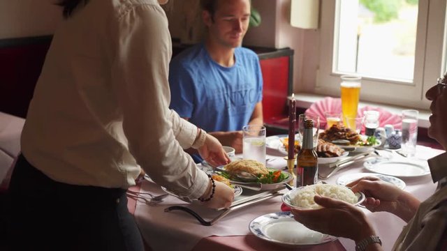 Waiter Or Waitress Serving Food At An Asian Restaurant To A Family Of Customers