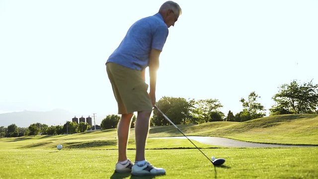 Awesome Slo-Mo shot of a man about to drive a golf ball off of the teebox. Cinematic sun flares can be seen behind the man.