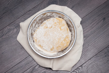The ball of raw dough for pizza or bread in metal plate on wooden background. Flat lay, top view.