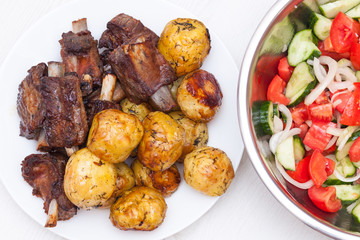 Sticky beef short ribs. BBQ ribs with potatoes and salad with tomatoes and cucumbers on white wooden background. Top view, flat lay.