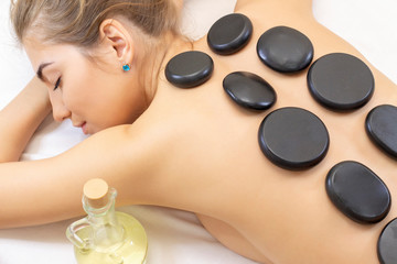 Obraz na płótnie Canvas Spa hot stone massage. Professional beautician massaging female back by stones. Relaxed girl enjoying body treatment at wellness center
