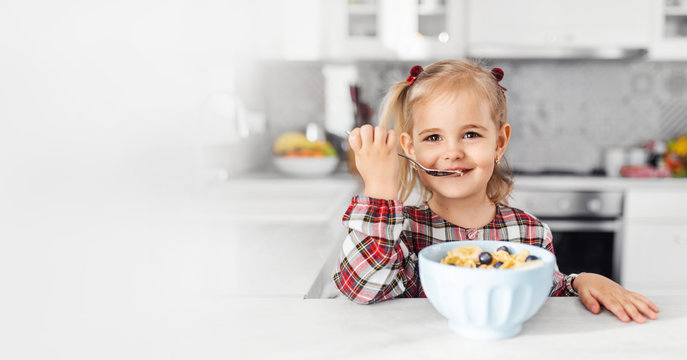 Beautiful little girl having breakfast with cereal, milk and banana in kitchen