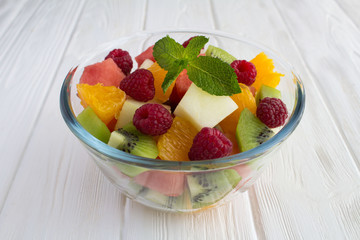 Fruit  salad in the glass bowl on the white wooden background. Closeup.
