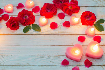 red roses and burning candles on wooden white background