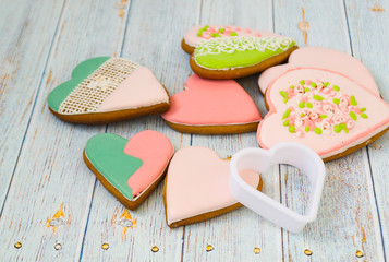 Pink and colored gingerbread and honey cakes and heart-shaped cookies lie in a messy pile on a light wooden background. Nearby are white molds for baking. Place for text. The concept of love, mother's