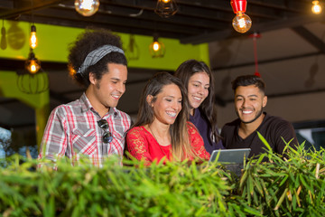 Young professionals are working outside the office at at cafe.  They are using a smartphone and a tablet. They are is smiling.