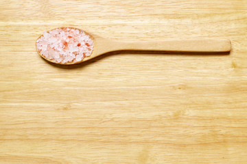 Himalayan pink salt in crystals in wooden spoon with wood background and copy space. Top view