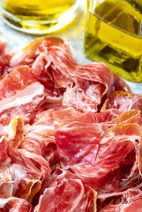 Appetizing slices Iberian ham in the foreground as a texture. Olive oil. Raw meat that becomes an article of haute cuisine and gastronomic luxury, through a process of raw salting and natural curing.