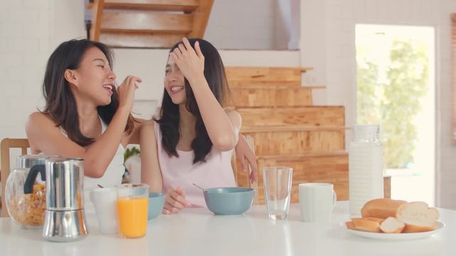 Asian Lesbian lgbtq women couple have breakfast at home, Young Asia lover female feeling happy drink juice, cornflakes cereal and milk in bowl on table in kitchen in the morning concept. Slow motion.
