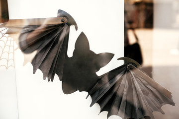 Flying scary bat and spider web on window in city street, holiday decoration of store fronts....