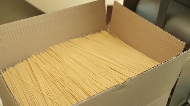 Packing pasta at the factory. Line for packaging pasta in plastic bags. Worker packs spaghetti in cardboard boxes. Large cardboard boxes with spaghetti. Packing workshop at a pasta factory.
