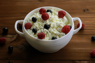 Bowl with cottage cheese and fresh berries on wooden background