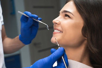 smiling happy brunette woman patient examined by dentist in blue gloves using dental mirror and...