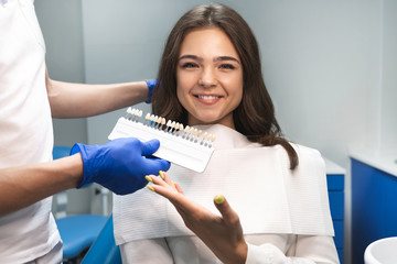 dentist in blue gloves showing tooth enamel scale to smiling woman patient for teeth bleaching...