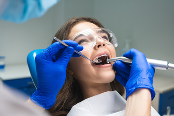dentist in mask filling the patient's root canal while she is lying on dental chair wearing safety...