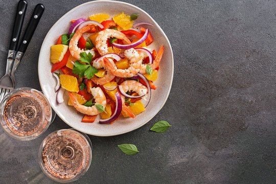 Ceviche with shrimps and orange, two glasses of pink sparkling wine, dark rustic background. Top view, copy space.