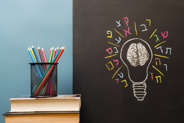 Book, pencils and light bulb with human brain and Hebrew letters on chalkboard