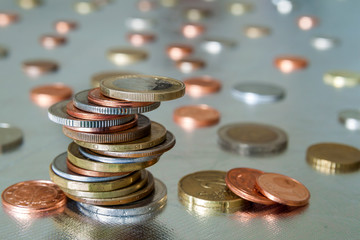 Pile of shiny coins different sizes and colors stacked unevenly on each other on colorful blurred blue abstract background. Money saving and financial risk concept.