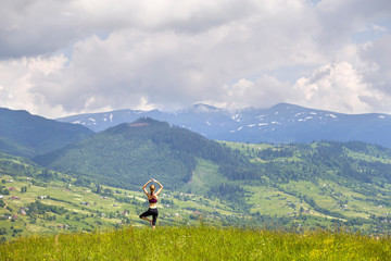 Fototapeta na wymiar Attractive slim young woman doing yoga exercises outdoors on background of green mountains on sunny summer day.