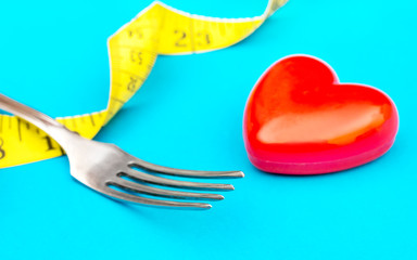 Fork with measuring tape and red heart on blue. Healthy lifestyle concept.