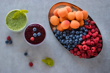 Fruit and berry smoothies and green smoothie. Fresh apricots, raspberries and blueberries on an oval metal plate. Gray background.