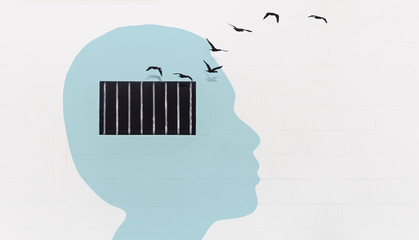 Free your mind concept and think out of the box concept, light blue human head with security window bar on the white wall with birds flying out from the window