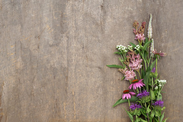 Horizontal image of a bunch of fresh cut perennial flowers in shades of pink and white on a weathered wood background, with copy space