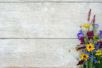 Horizontal image of a colorful bunch of bright summer flowers against a weathered wood background, with copy space