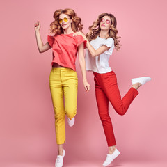 Two easy-going happy hipster Woman dance Fun in Stylish fashion colored red yellow pants. Beautiful excited Girl in summer Trendy outfit, sneakers jump laughing. Creative dancing fashionable concept