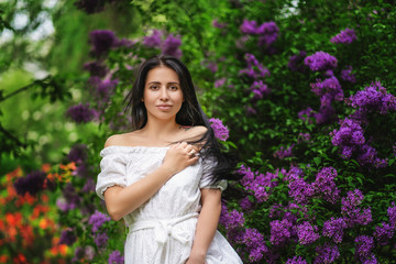 Spring portrait of stunning woman walking in the blooming lilac garden.