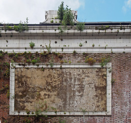 an old stone poster frame on the wall of a derelict cinema with plants growing out of a decaying...