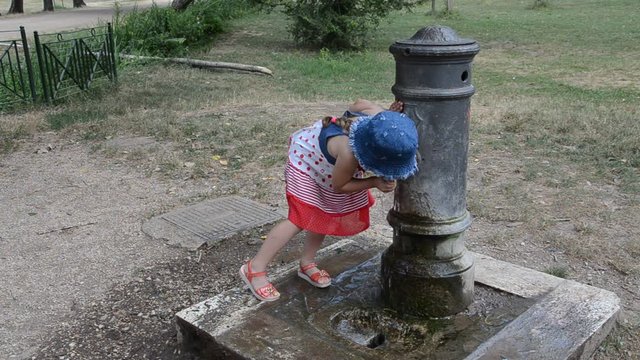 Little adorable baby girl drinks water from the drinking fountain of the roman nose on the streets of Rome
