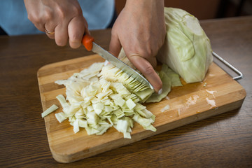 Female hands cut cabbage on a wooden plate on the table in the kitchen. Proper nutrition.