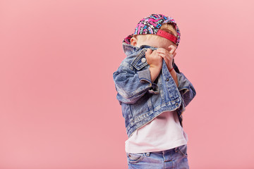 Little serious fashionable toddler boy in denim clothes and trendy cap. Isolated on pink background