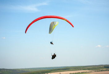Paragliding over the green field in summer sunny day. Two paragliders fly over green field near Dnister river in Ukraine.